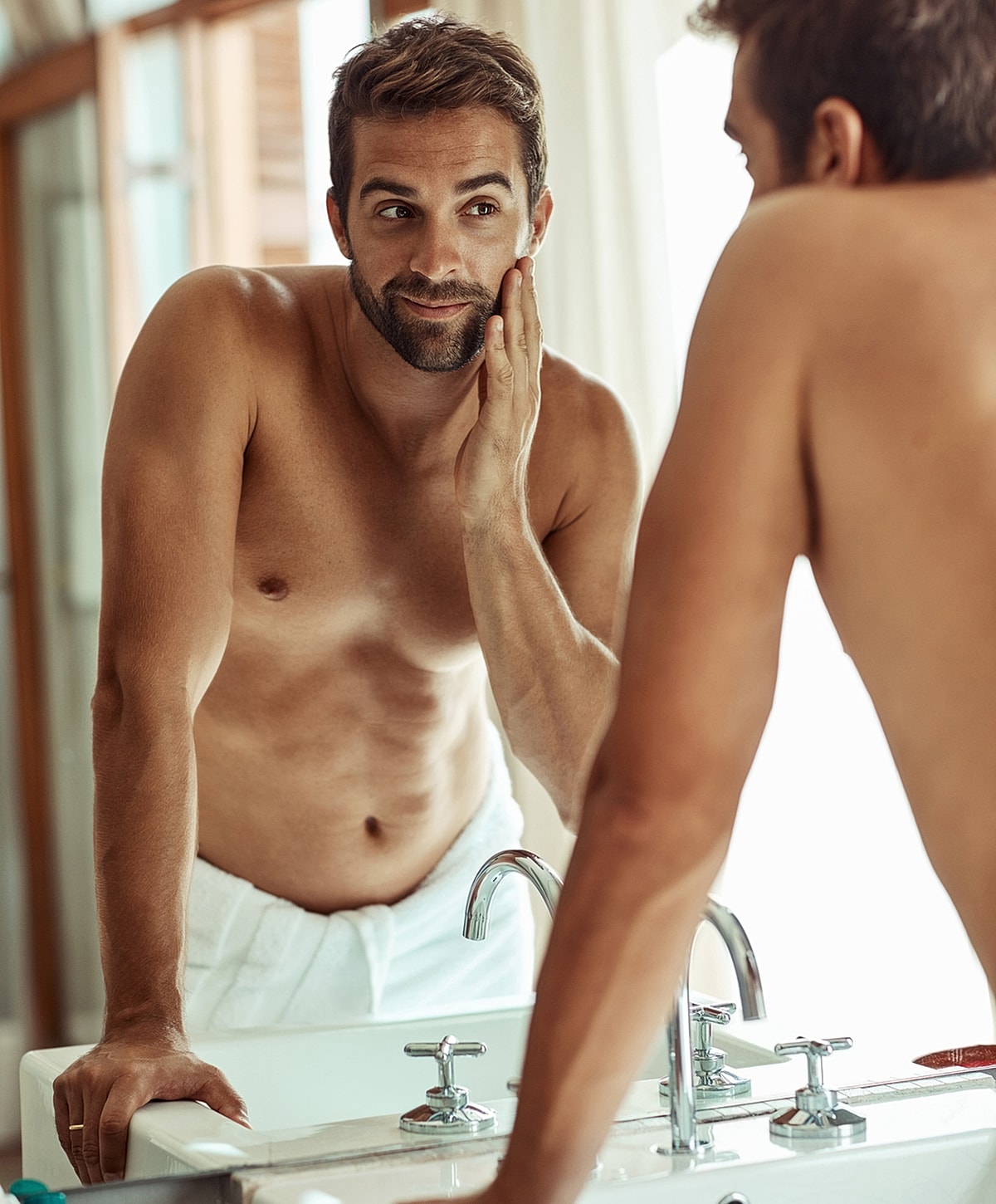 Man grooming himself in bathroom mirror reflection.