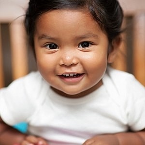 Smiling toddler with dark hair sitting happily.