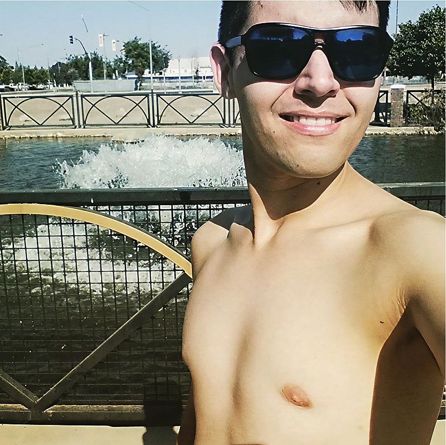 Man smiling by water fountain in sunlight.