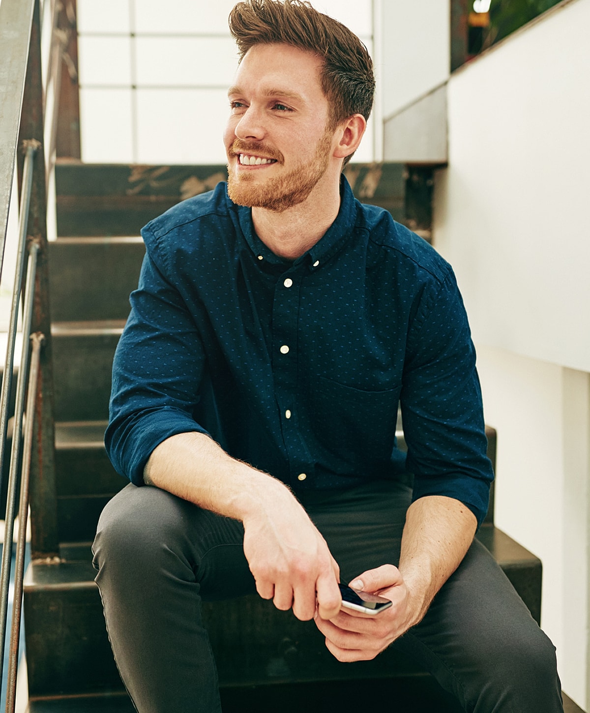 Man sitting on stairs with smartphone, smiling.