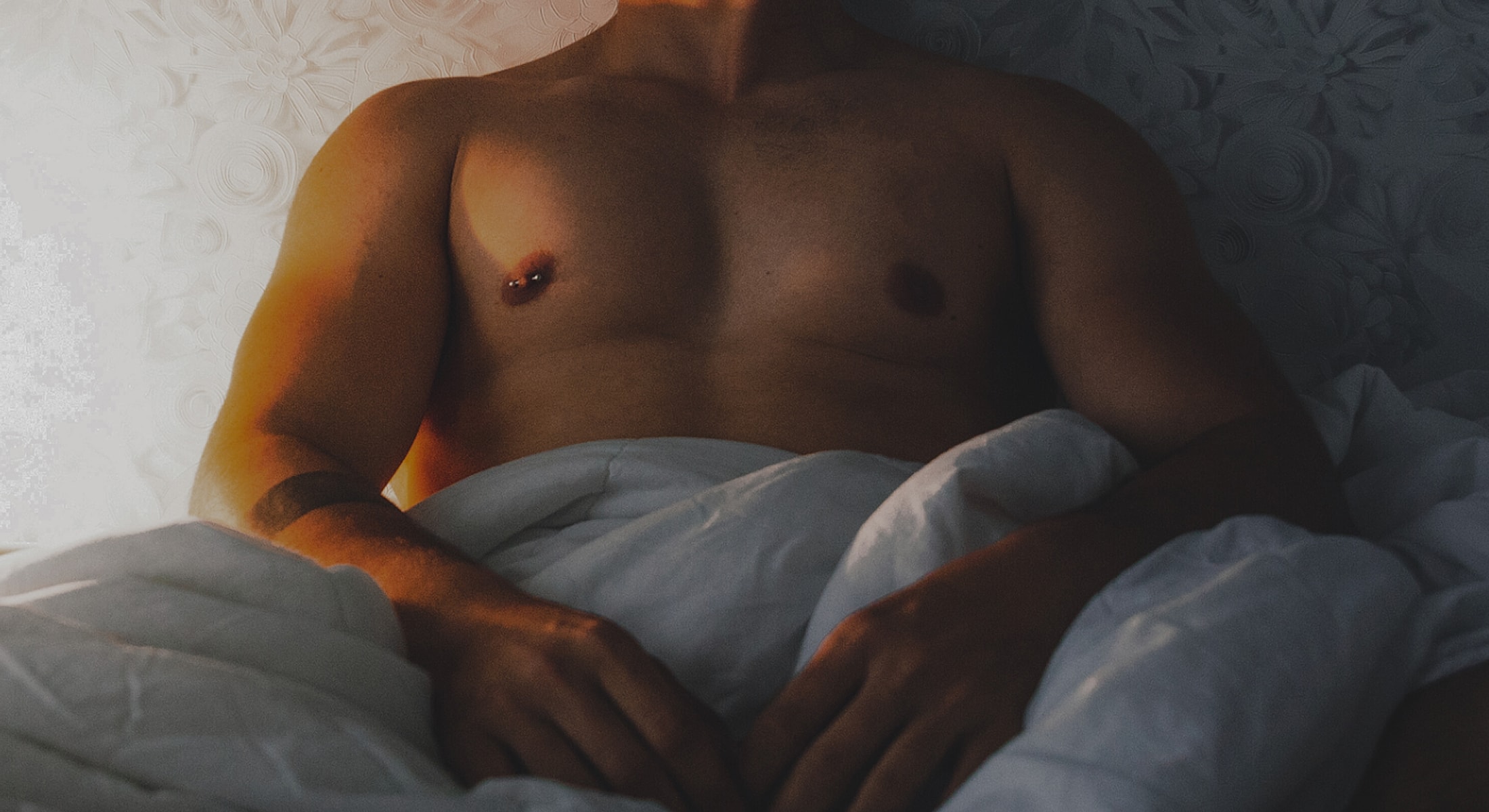 Man sitting in bed covered with a blanket.